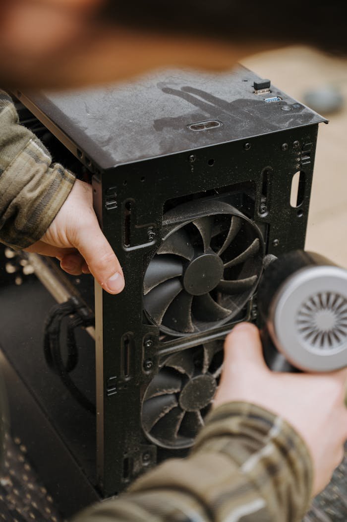 about-01 Hands cleaning dust from a computer fan using an electric air duster for maintenance.